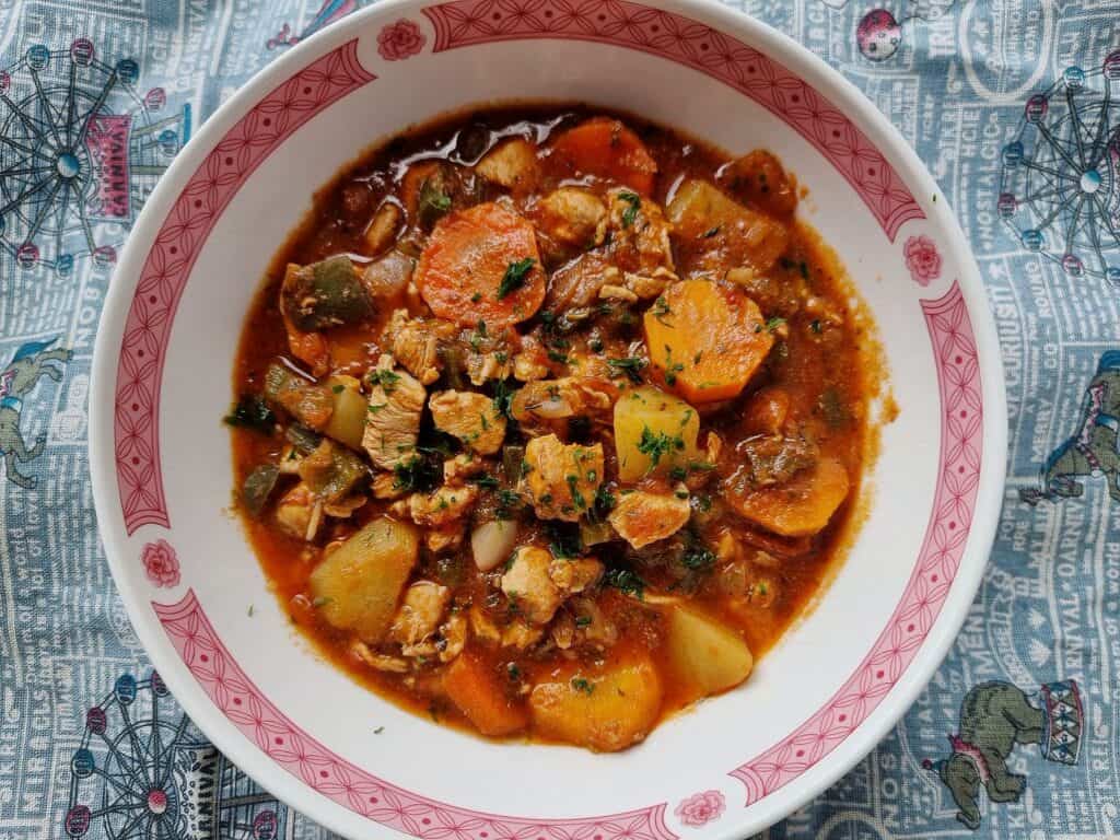 A turkish chicken stew Tavuk Sote that contain chopped boneless chicken breast with carrots and potatoes garnished with chopped parsley cooked in a tomato sauce served in a bowl.